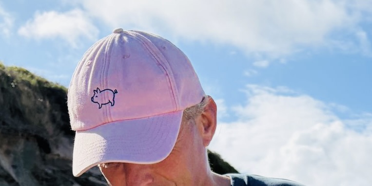 Someone wearing the pink Signature Tipsy Pig cap on the coast